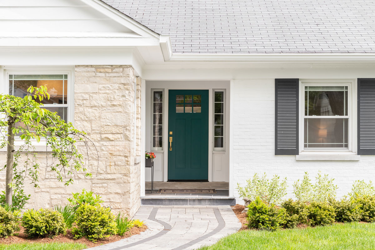 The front of a white house with a green door, stone entry, and a curved walkway.